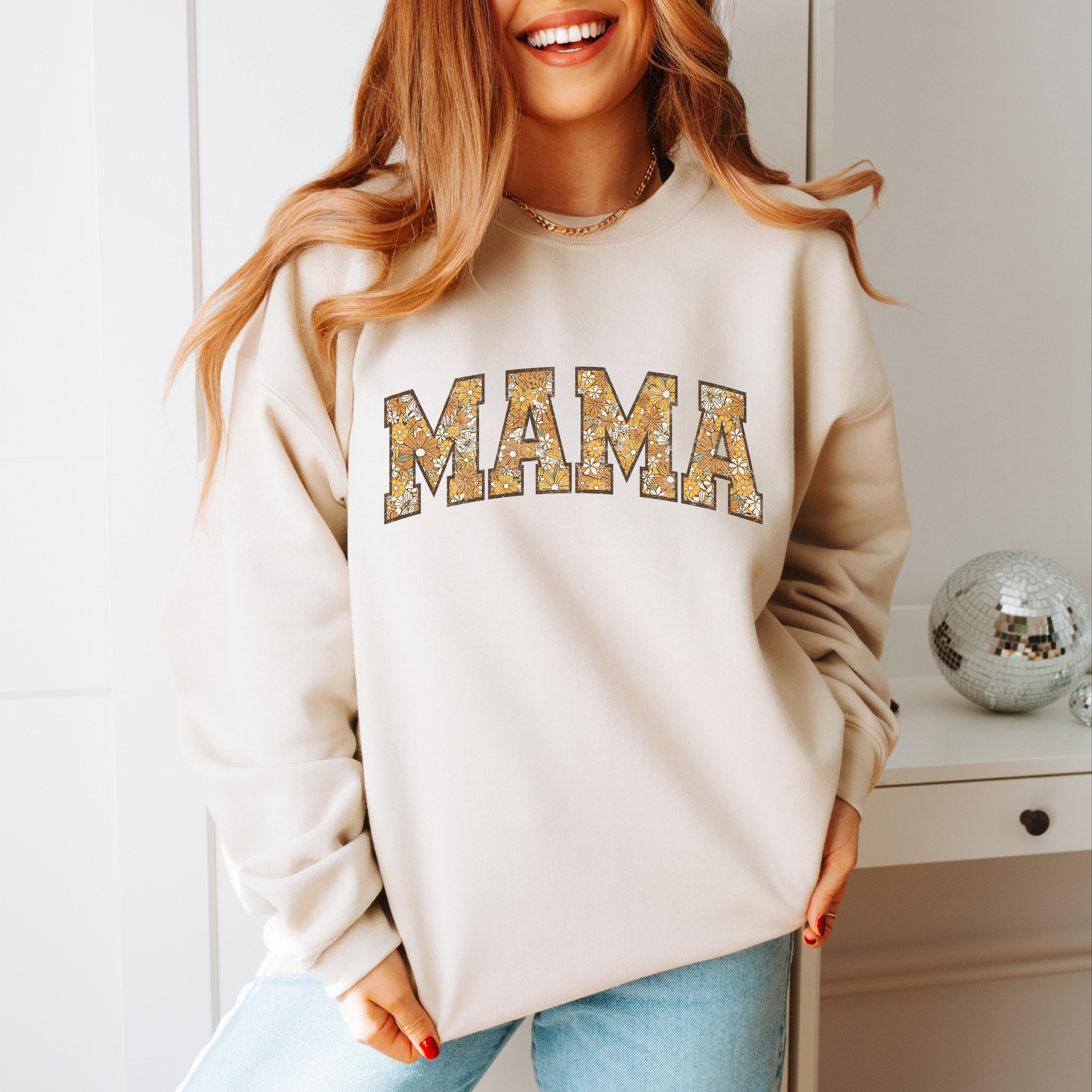 A soft, sand colored sweatshirt with the word Mama across the chest in a varsity jacket font and filled with floral patterns.