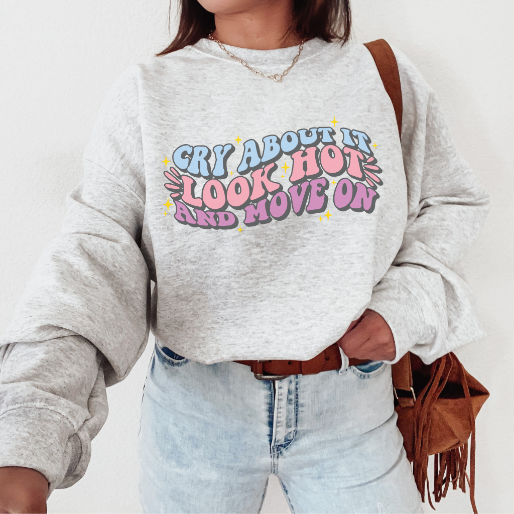 A light, grey sweatshirt with the words cry about it, look hot, and move on written in a colorful, graphic style and surrounded by small, yellow stars.