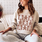A woman wearing a sand color sweatshirt featuring 9 cute gingerbread men.
